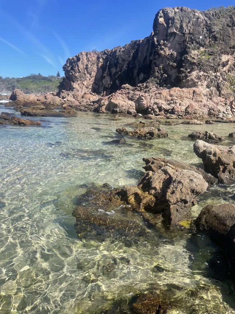 Clear rock pool water beneath a red rock headland